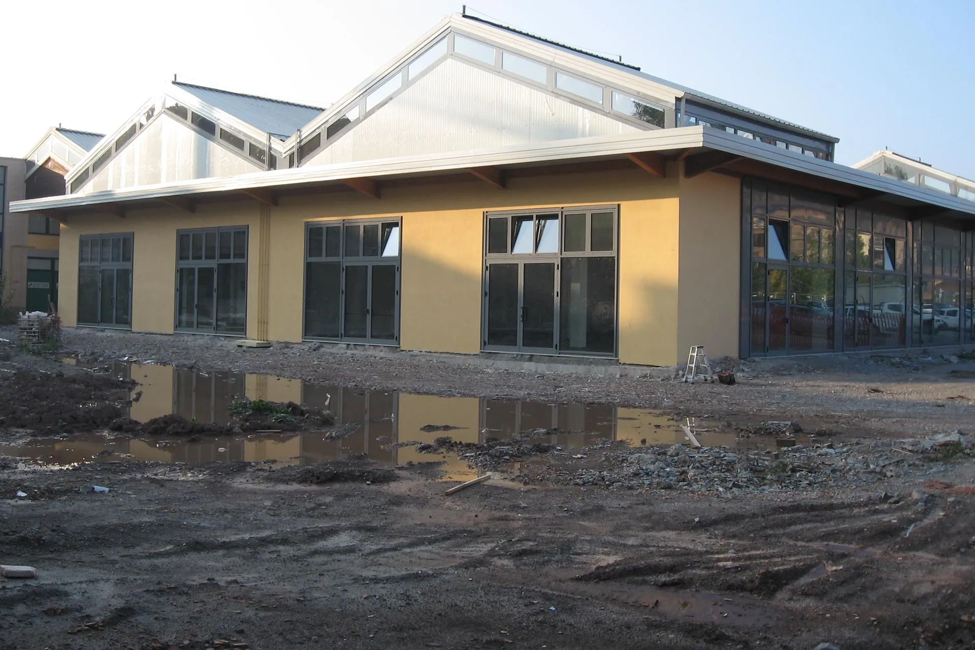 Capannone con facciata gialla e grandi serramenti in alluminio scuro, con il cantiere ancora aperto davanti.