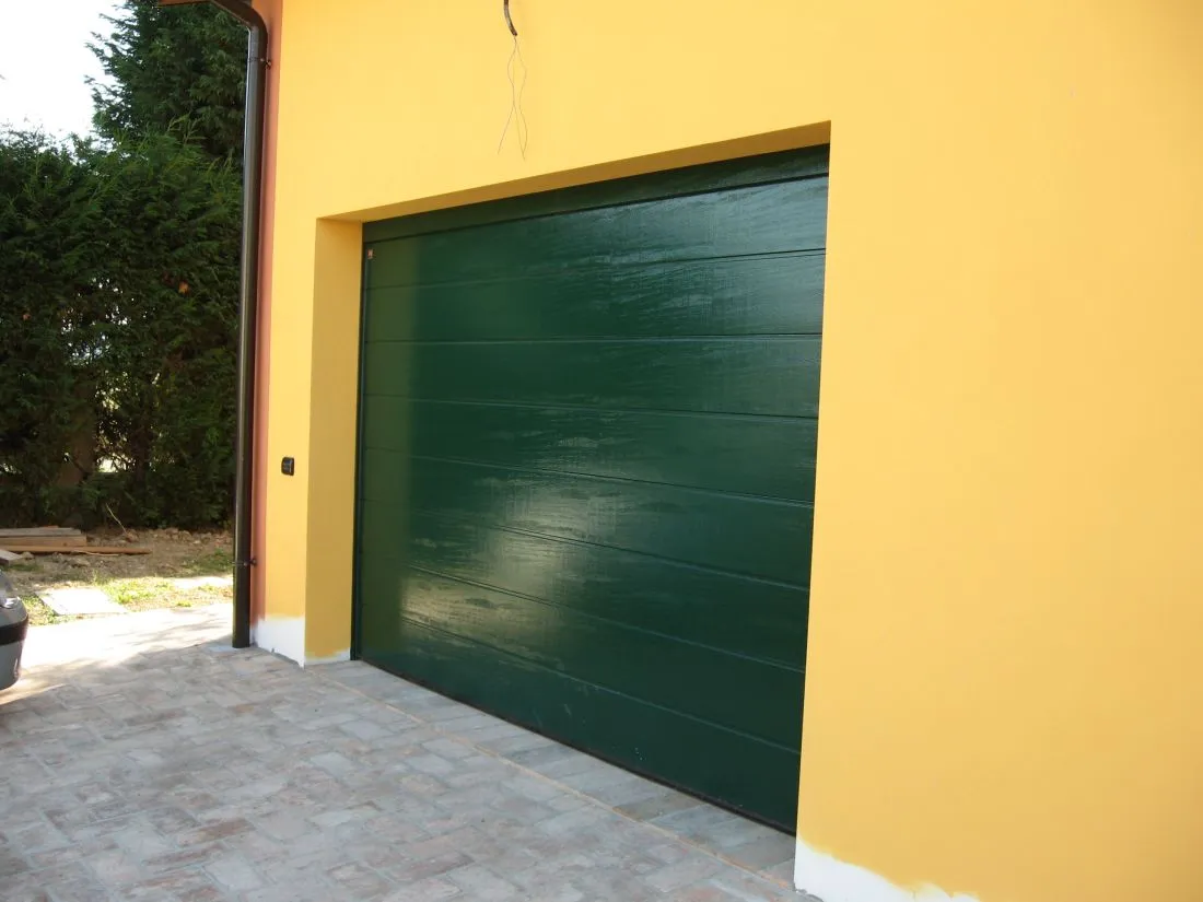 Portone sezionale verde scuro su una facciata gialla.