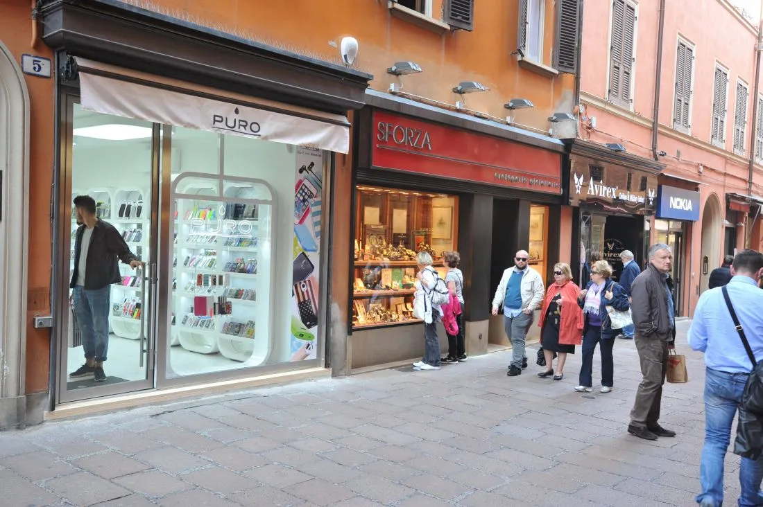 Vetrina di un negozio in via D'Azeglio a Bologna con telaio in acciaio inox, vista dalla strada con alcuni passanti.